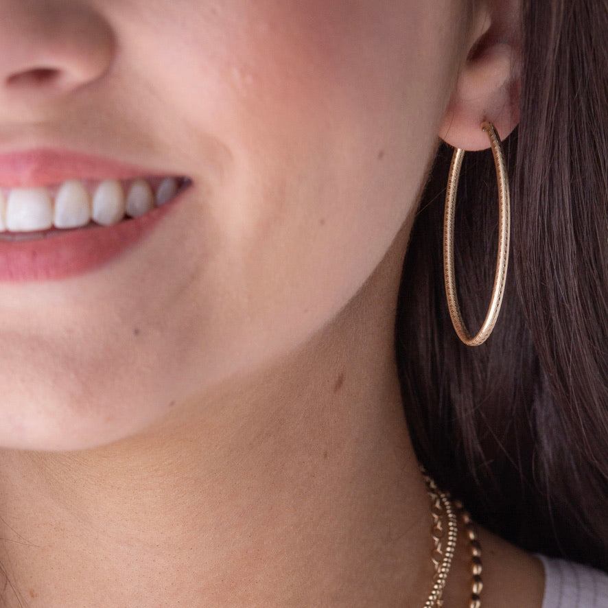 Model wearing large oval gold textured hoop earring with brushed finish detail