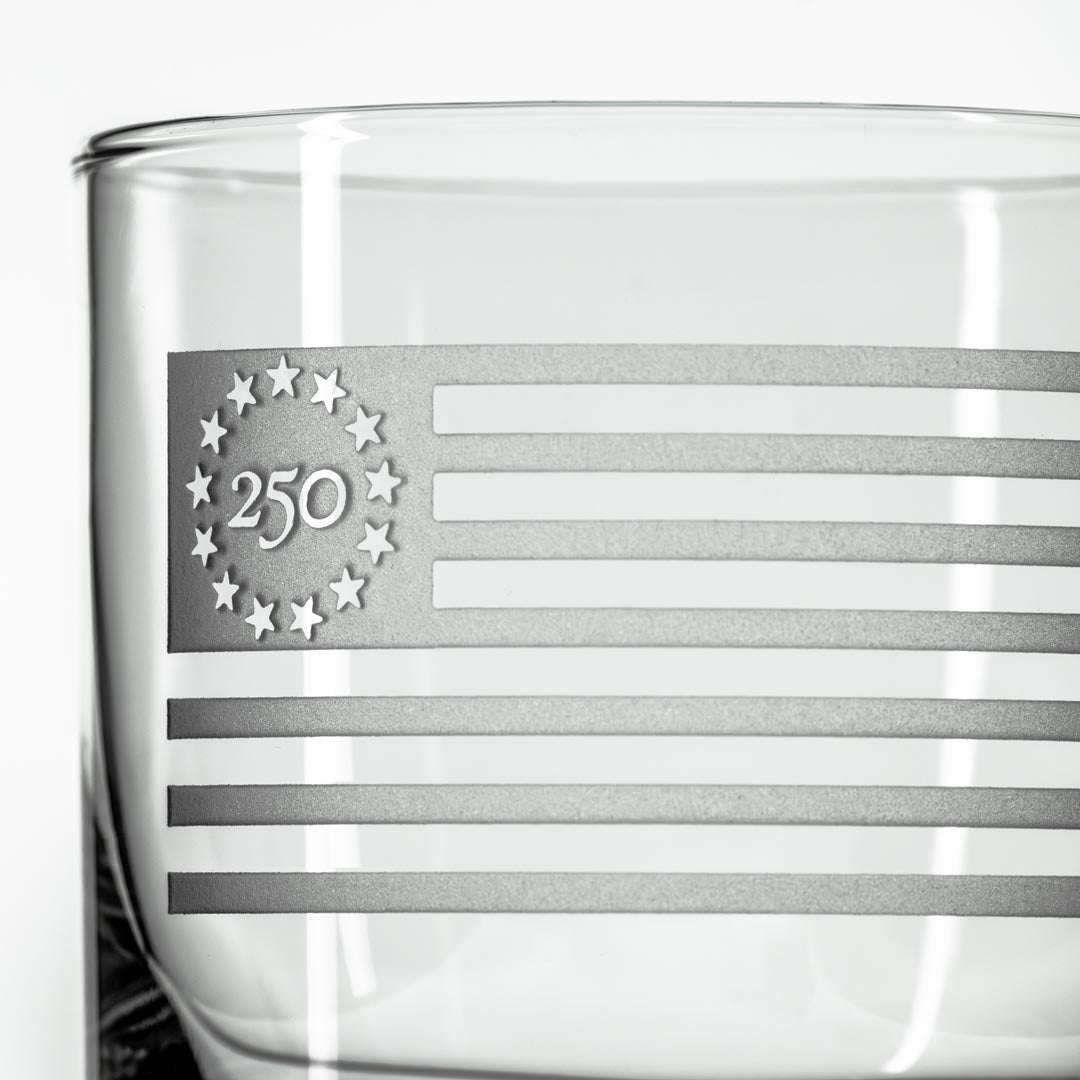 Close-up of clear whiskey glass with etched Betsy Ross flag design featuring 13 stars in circle and 250 text