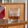 Clear whiskey glass with Betsy Ross flag design containing amber liquid on wooden surface
