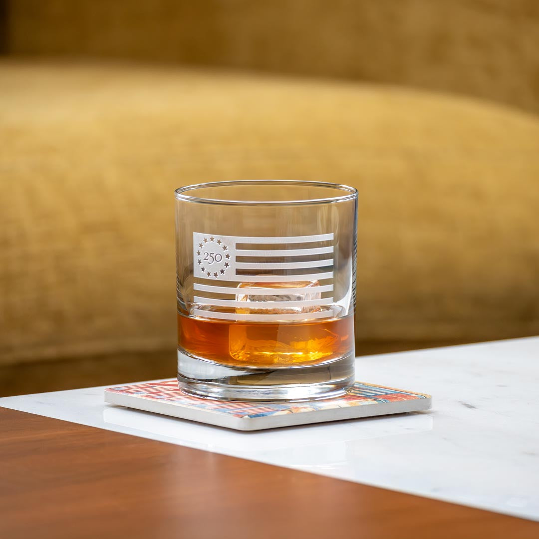 Clear whiskey glass with etched Betsy Ross flag design containing amber whiskey on napkin