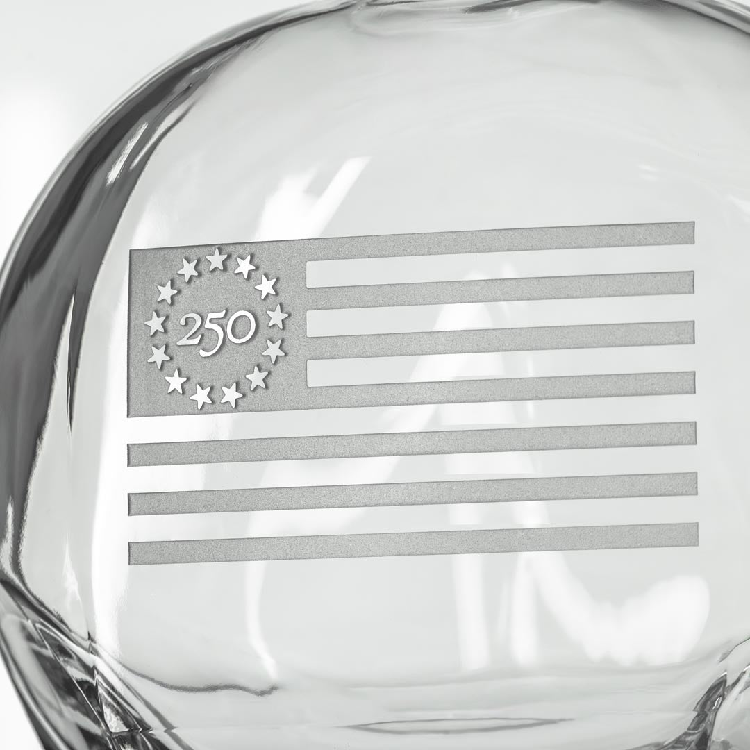 Close-up of clear glass whiskey decanter showing etched Betsy Ross flag with 13 stars and 250 commemorative marking
