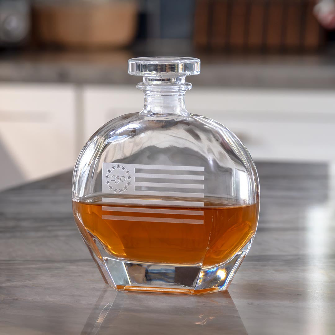 Clear glass whiskey decanter with etched American flag and 250 logo containing amber liquid