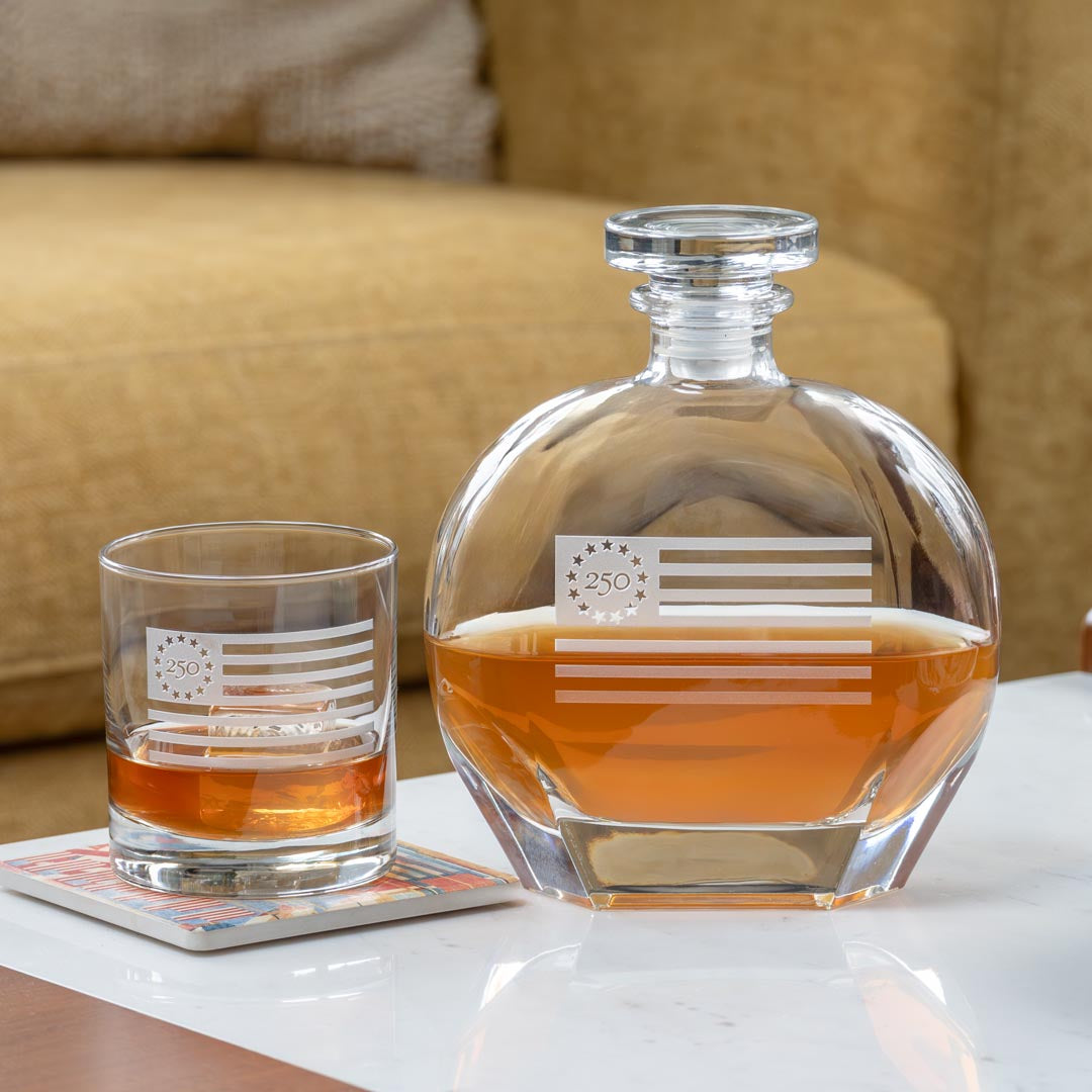 Clear glass whiskey decanter and matching glass with Betsy Ross flag design containing amber whiskey
