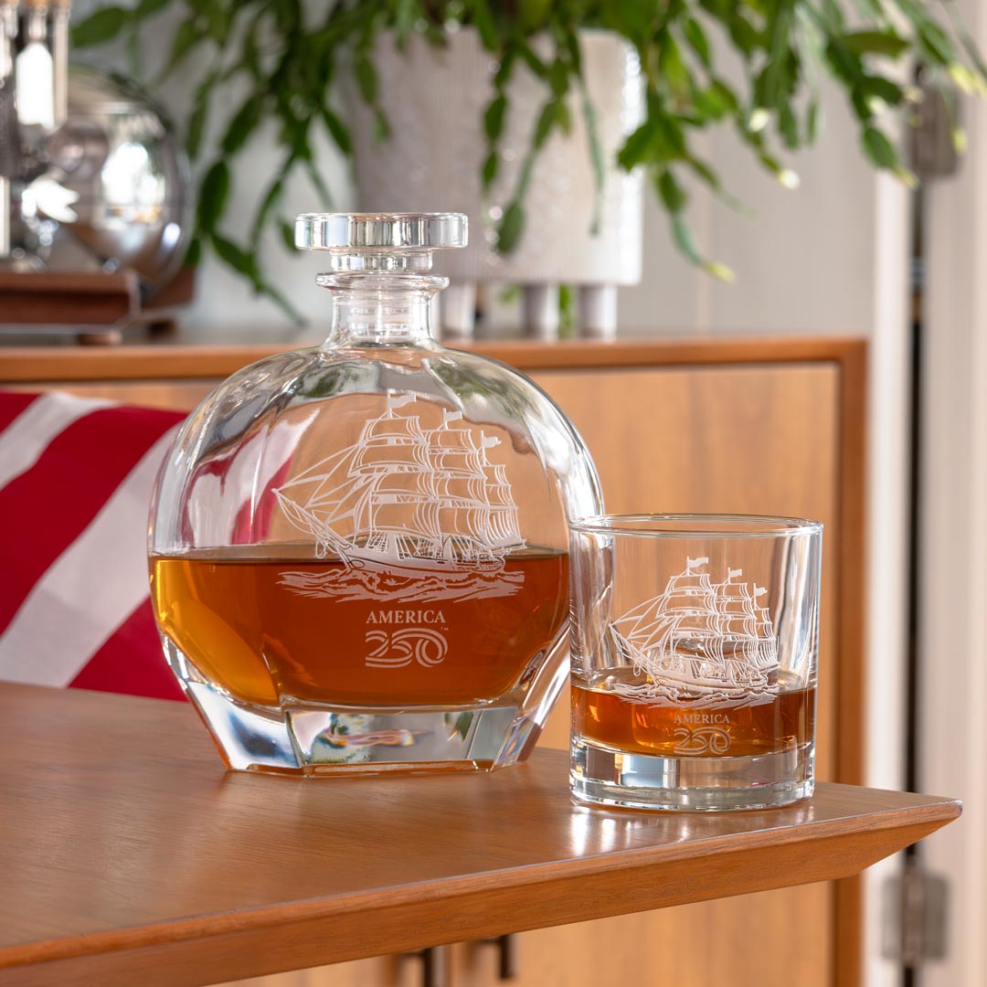 America250 tall ship whiskey decanter and rocks glass with amber liquid on wooden table
