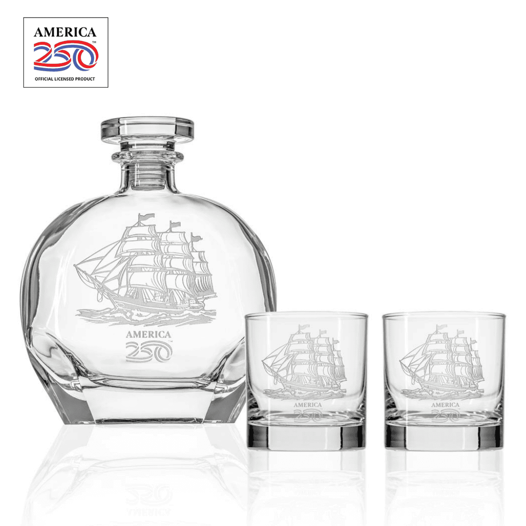 Clear glass whiskey decanter and two rocks glasses with etched tall ship design and America 250 logo