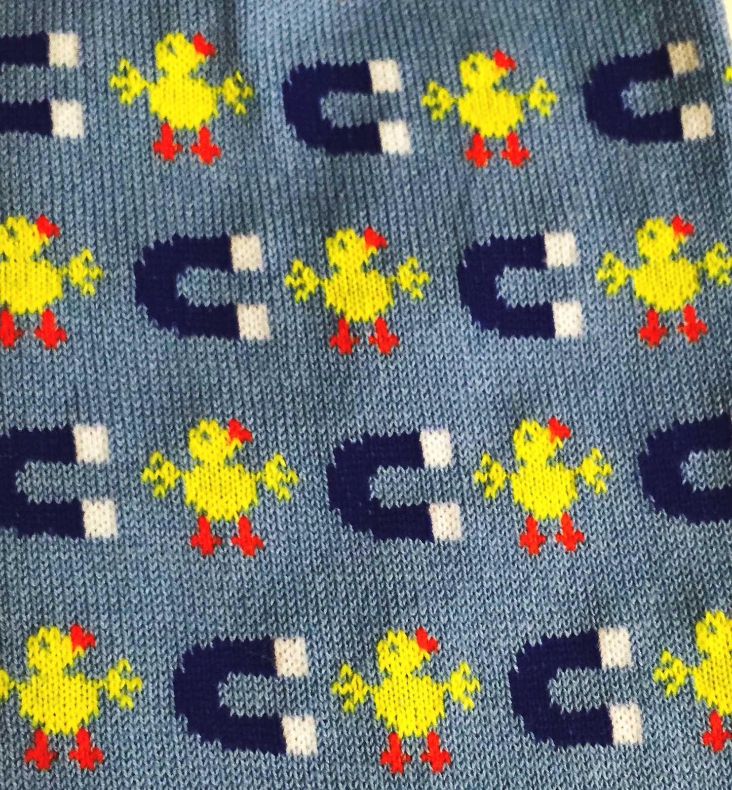 Blue knitted socks with repeating pattern of yellow chicks and dark blue horseshoe magnets on light blue background
