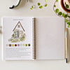 Open watercolor workbook showing garden cottage tutorial with paint swatches and blank practice page