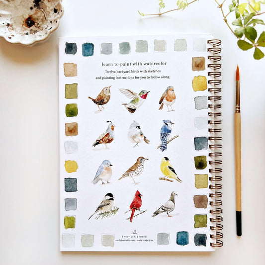 Emily Lex Studio watercolor workbook showing twelve backyard birds with color swatches and painting brush